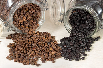 Natural roasted coffee beans and torrefacto coffee beans get out of overturned and open glass pots
