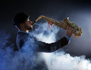 Fototapeta na wymiar Elegant saxophonist plays jazz on dark background in a smoke