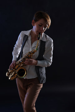 Attractive woman plays saxophone on black background