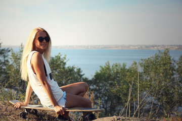 Young woman with skating board on the riverside