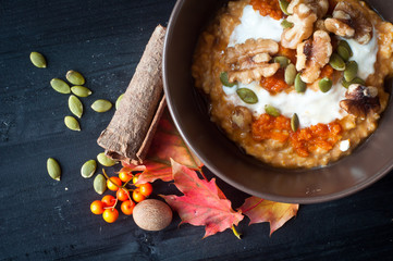 Healthy breakfast of pumpkin porridge with Greek yogurt, pumpkin seeds and walnuts, the perfect start to an autumn fall morning.Served with a scattering of pumpkin seeds, spices and autumn fall leaves
