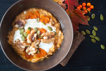 Healthy breakfast of pumpkin porridge with Greek yogurt, pumpkin seeds and walnuts, the perfect start to an autumn fall morning.Served with a scattering of pumpkin seeds, spices and autumn fall leaves