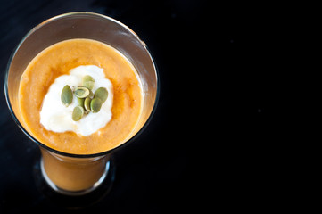 Healthy breakfast smoothie milkshake of blended pumpkin, yogurt,banana,almond milk and topped with greek yogurt and and pumpkin seeds. Isolated on black.