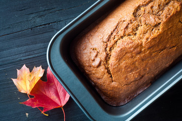 Freshly baked pumpkin bread cake in a baking tin. Served with a scattering of autumn fall leaves.