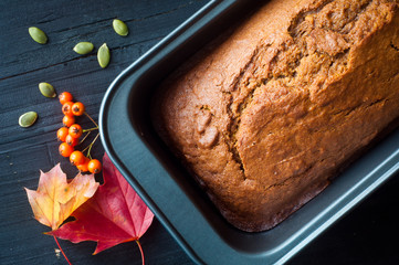 Freshly baked pumpkin bread cake in a baking tin. Served with a scattering of pumpkin seeds and some autumn fall leaves and berries.