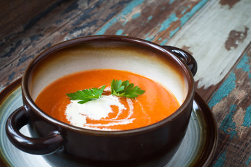 Bowl of home made pumpkin soup topped with a little cream and fresh parsley. Served on a rustic wooden table with freshly baked crusty bread.