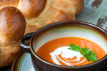 Bowl of home made pumpkin soup topped with a little cream and fresh parsley. Served on a rustic wooden table with freshly baked crusty bread.