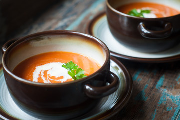 Bowl of home made pumpkin soup topped with a little cream and fresh parsley. Served on a rustic wooden table with freshly baked crusty bread.