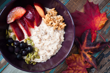 Healthy home made oats porridge topped with blueberries, walnuts and fresh plums. Served on a rustic wooden table.