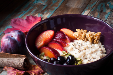 Healthy home made oats porridge topped with blueberries, walnuts and fresh plums. Served on a rustic wooden table.