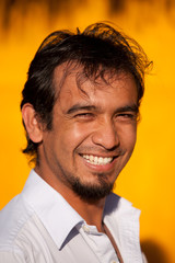 Adult male with a genuine smile,basking in natural light,photographed against a vibrant yellow wall.