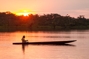 An indigenous tribe in Ecuador's Amazonia region paddles a traditional canoe through the lush...