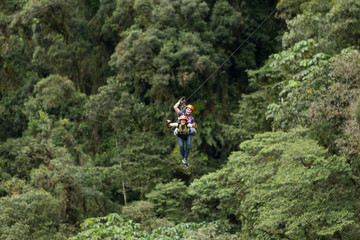 Fototapeta premium A woman wearing sports gear slides down a zipline through the lush jungle canopy, holding onto a rope as she speeds along the line.