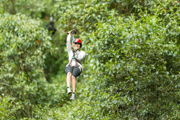 A woman in a helmet and harness glides on a zipline through a dense green jungle canopy in Ecuador, gripping the cable mid-flight on a thrilling canopy zipline adventure in the rainforest. © Ammit