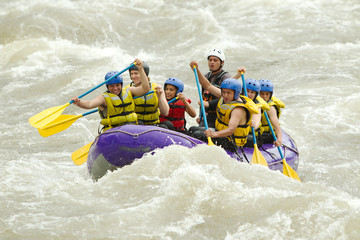 A group of energetic people in a white raft, navigating through green water, embarking on an exciting team adventure.