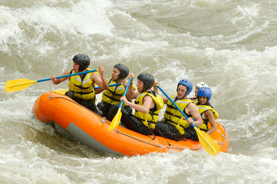 A group of men navigating a white water rafting course, competing in an extreme boating sport on rough waters.