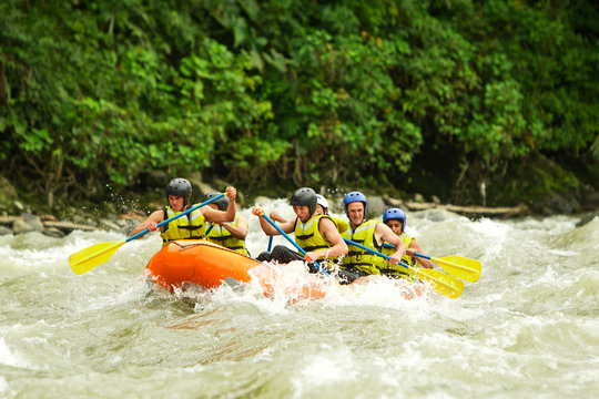 A group of men in an orange raft paddle through turbulent white-water rapids surrounded by lush green jungle in Ecuador, splashing water and teamwork capturing an exciting adventure in nature.