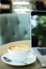 Hot art Latte Coffee in a cup on wooden table and and laptop in