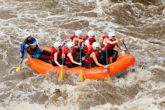 A group in red life jackets and helmets paddle a bright orange raft through churning whitewater rapids on a guided rafting trip in Ecuador, splashing waves and teamwork.
