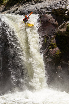 A daring kayaker in a yellow kayak plunges down a powerful waterfall over dark moss-covered rocks in Sangay National Park, Ecuador, the splash capturing the thrill of extreme whitewater kayaking.