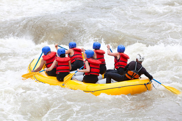 A diverse group of women paddle a white-water raft together, demonstrating teamwork as they navigate through thrilling rapids on a river.