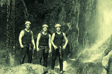 Fototapeta premium Three young men dressed in sport suits posing against a breathtaking waterfall,showcasing their athletic prowess and love for adventure.