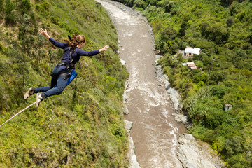Naklejka na ściany i meble A girl in Banos, Ecuador, stands on a cliff looking scared before bungee jumping with people watching and cheering on her adventurous activity.
