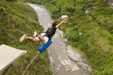A group of excited travelers bungee jumping off a bridge in Ecuador, surrounded by lush greenery and a roaring waterfall below.