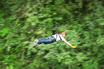A man flying through the forest on a secure zipline, surrounded by nature and other adventurous people, feeling the thrill of speed and excitement.