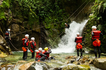 A group of adventurous people having fun zip-lining through a canyon in Ecuador, surrounded by waterfalls and enjoying the thrilling adventure. - obrazy, fototapety, plakaty