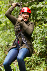 A black zipline wire stretches through the jungle as a girl flies on an adventure, feeling the thrill of the flight and having fun.