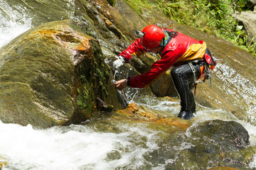 Expert instructor meticulously drilling holes for a thrilling new canyoning route at the breathtaking Chama Waterfall in Ecuador's lush wilderness.