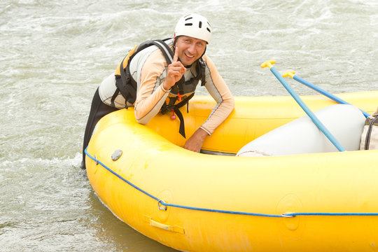 A man in a white rafting boat, guided by an expert, navigates the rushing river while floating on a tube, surrounded by glistening water.
