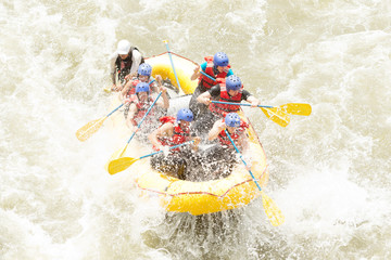 A team of men and a woman navigate through white water rapids on a raft, facing an...