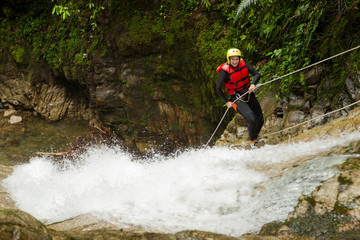 Obraz premium A group of women racing down a waterfall while rappelling during a canyoning descent, each person securely attached to a rope.