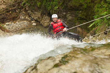 A daring human in climbing equipment rappels down a waterfall in a canyon, experiencing an adrenaline rush while canyoning.