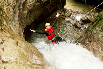 A woman in waterproof gear rappelling down a canyon wall next to a stunning waterfall, surrounded...