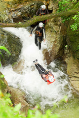 A small river cuts through a rugged canyon as an extreme canyoning enthusiast in a harness navigates the rocky terrain.