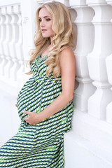 Beautiful pregnant woman with long blond hair in elegant dress posing in summer day
