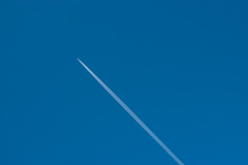 Fototapeta na wymiar A distant airplane with a contrail