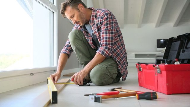 Cheerful man at home installing new wooden floor