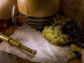 Still life with a bunch of grapes, a glass of wine, a barrel and a map, on a wooden table