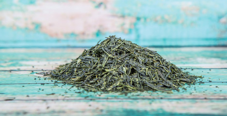 Dried green tea leaves over wooden background