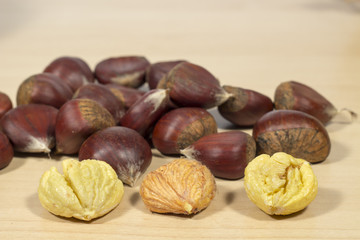 Several peeled chestnuts, one with pellicle,  in front of other ones in shell