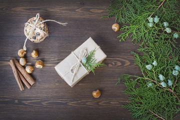 Christmas gift, chocolate cookies, nuts, cinnamon, pine cones and green arborvitae branch on a wooden table