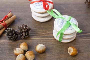 Christmas cookies with ribbons, apples, nuts, cones, cinnamon and green arborvitae branch on a wooden table.