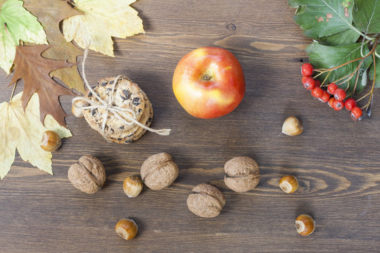 Apple, cookies with chocolate, nuts, mountain ash and red autumn leaves on a wooden table