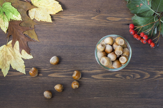 Hazelnuts, mountain ash, red and yellow autumn leaves on a wooden background