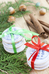 Christmas cookies with ribbons, apples, nuts, cones, cinnamon and green arborvitae branch on a wooden table.