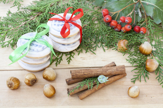 Christmas cookies with ribbons, apples, nuts, cones, cinnamon and green arborvitae branch on a wooden table.